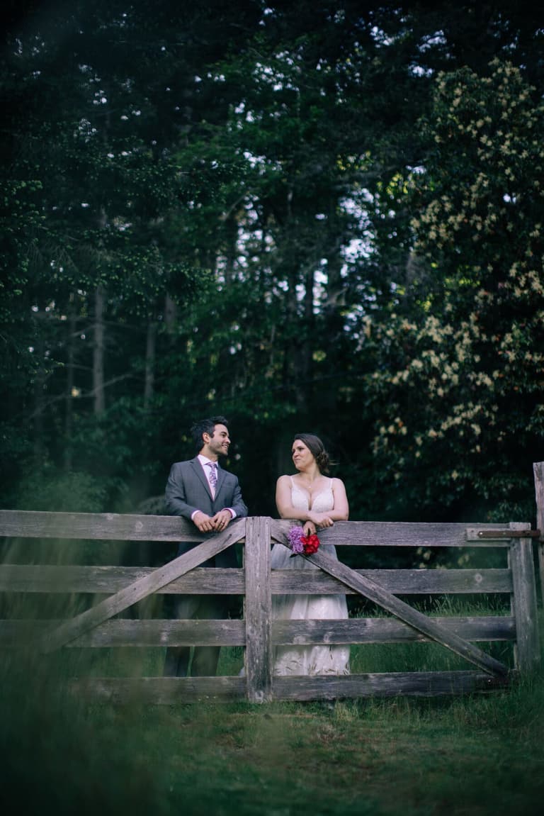 Smiles across a weathered fence, bouquet resting on the rail
