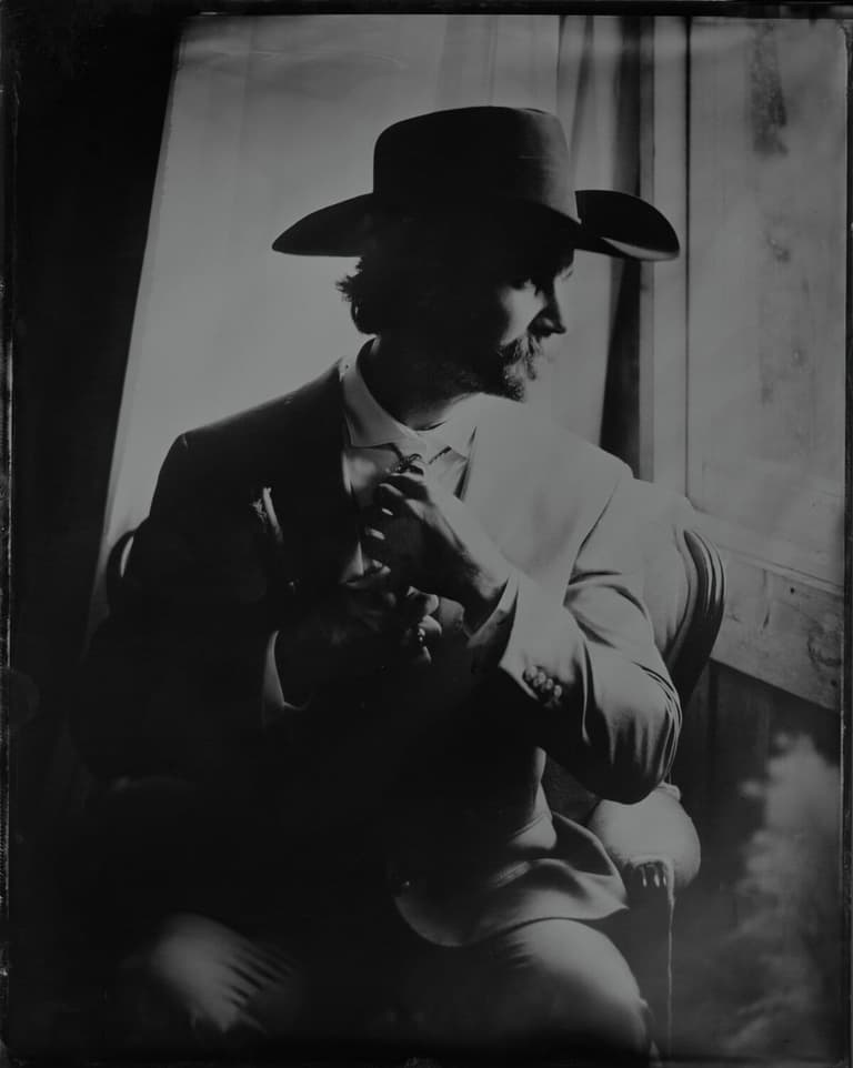 Shadowed tintype of a man in a cowboy hat adjusting his tie