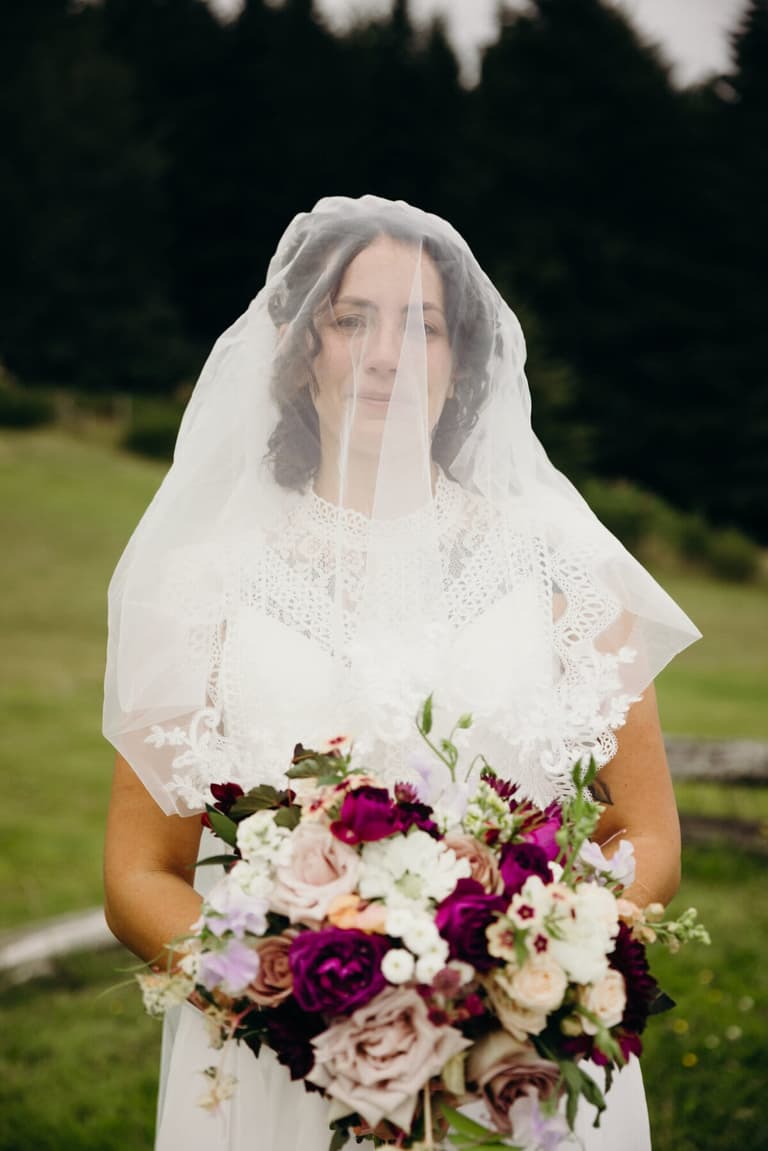 Veiled bride holding a plum and blush rose bouquet