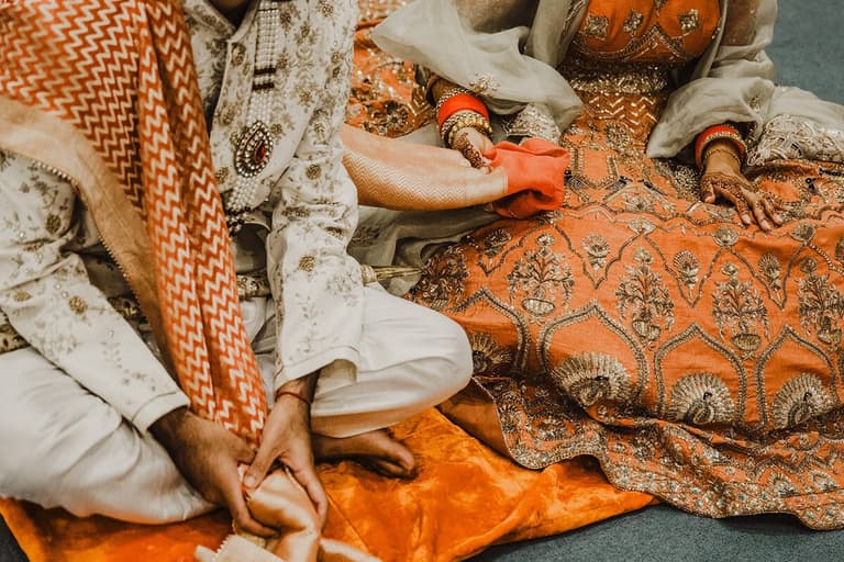 Embroidered orange and cream attire during a South Asian wedding ritual
