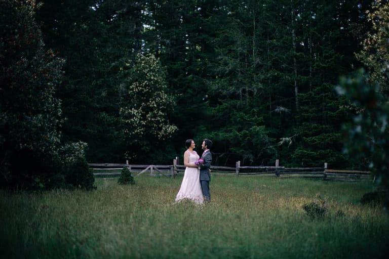 Couple facing one another in a clearing before towering evergreens