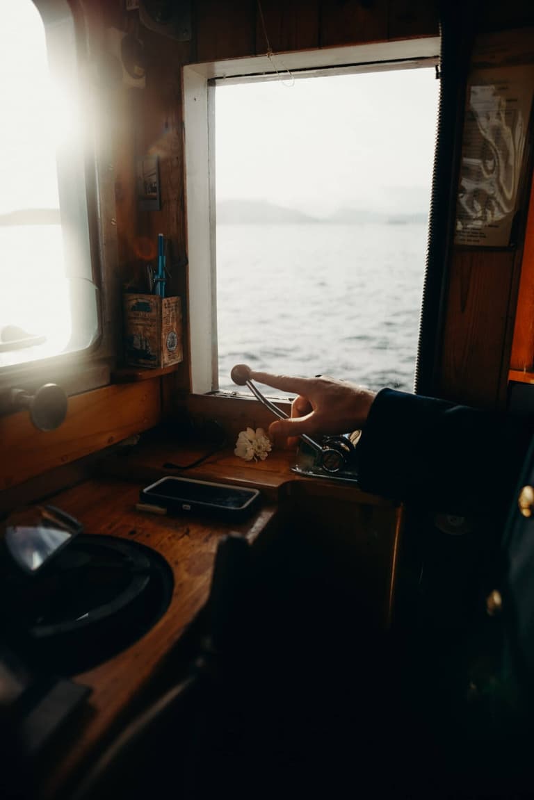 Hand resting on the controls inside the sunlit wooden wheelhouse