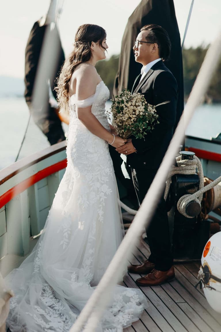 Bride and groom facing each other on deck, baby's-breath bouquet between them