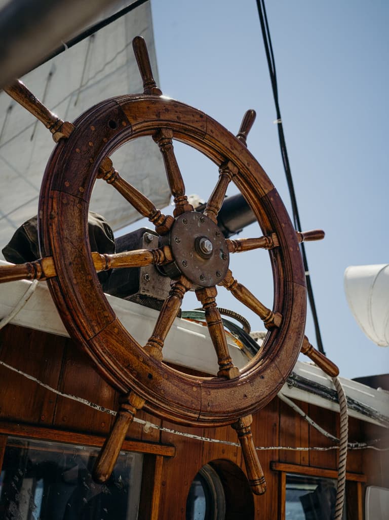 Weathered wooden ship's wheel against sail and summer sky