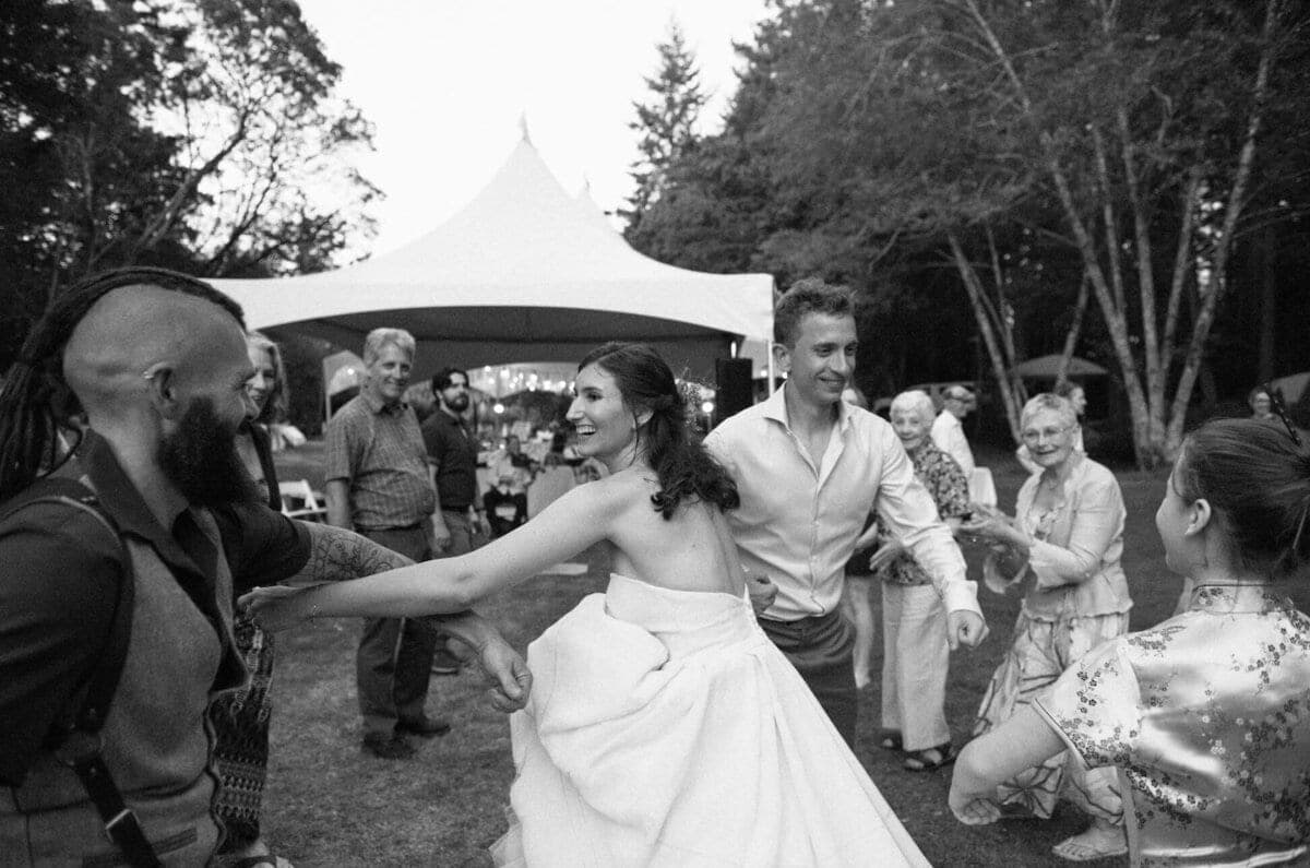 Bride and groom dancing outdoors under a tent with evergreen trees and guests at a Gulf Islands wedding
