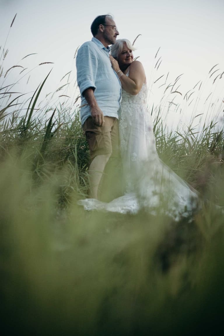 Silver-haired couple embracing in tall grass at dusk