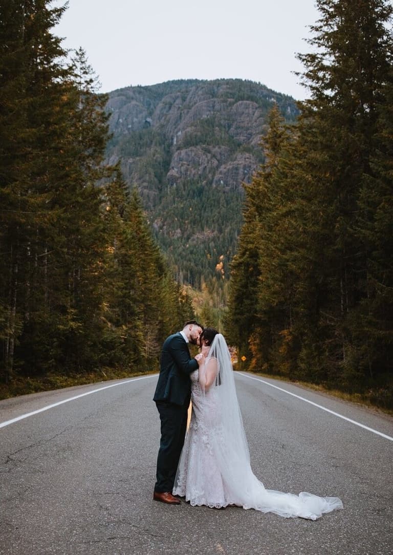Eloping couple embracing on an evergreen-lined mountain highway
