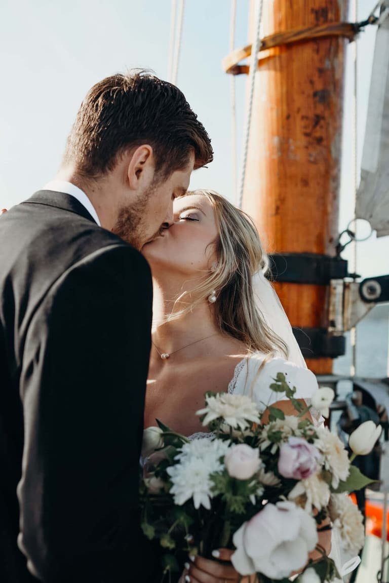 Newlyweds kissing beside the mast with a blush and white bouquet