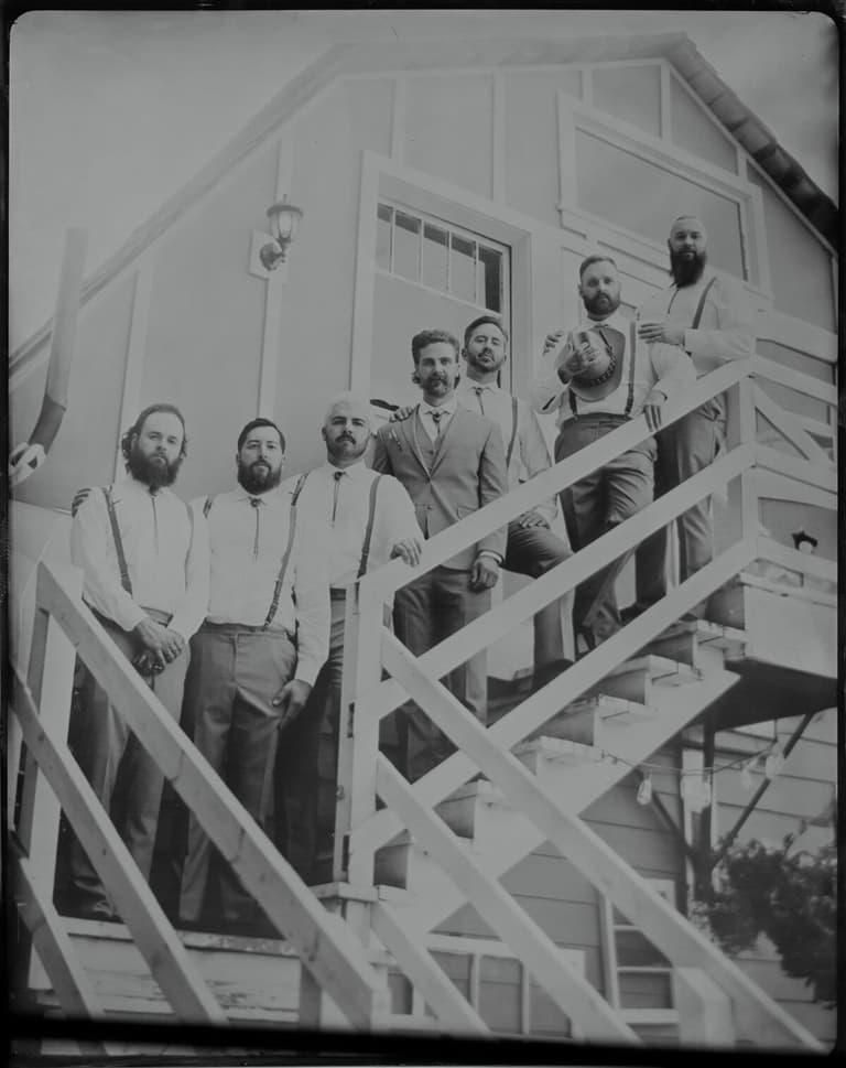 Bearded groomsmen in suspenders lining an exterior staircase, tintype style