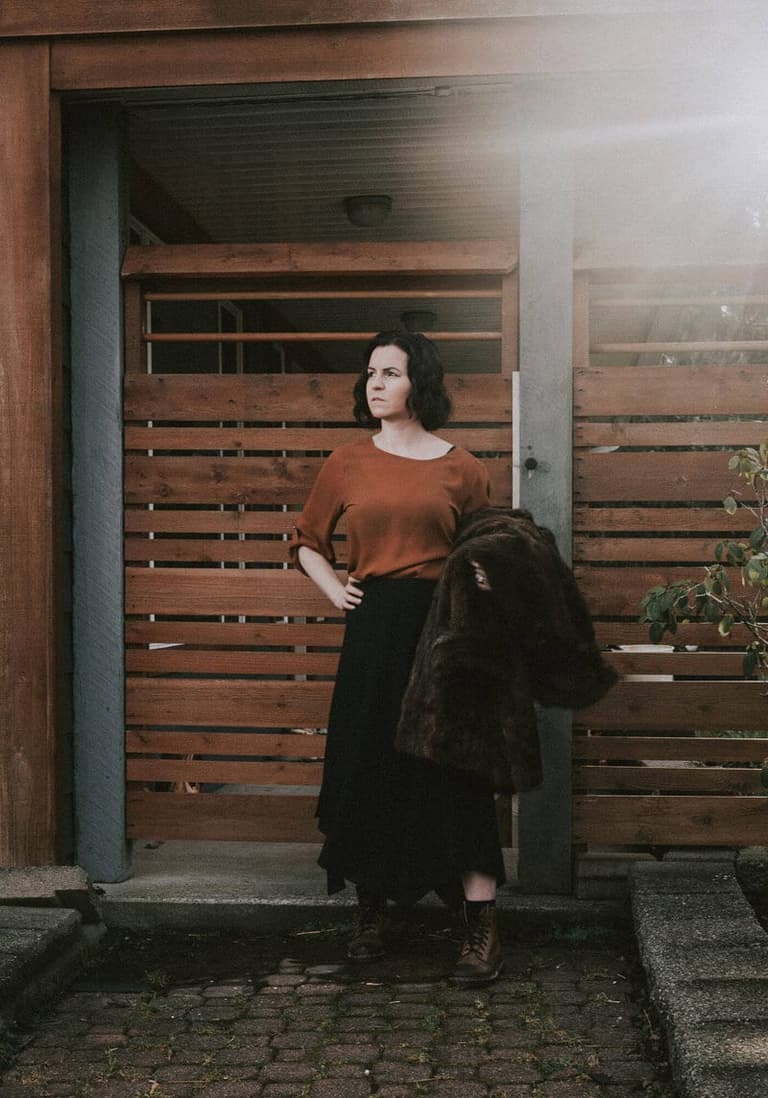 Photographer Jen McLeod holding a fur coat beside cedar slats