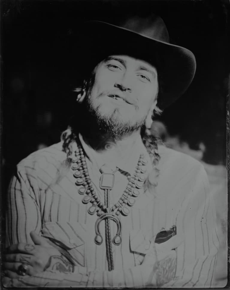 Grinning cowboy with braids and a silver squash-blossom necklace