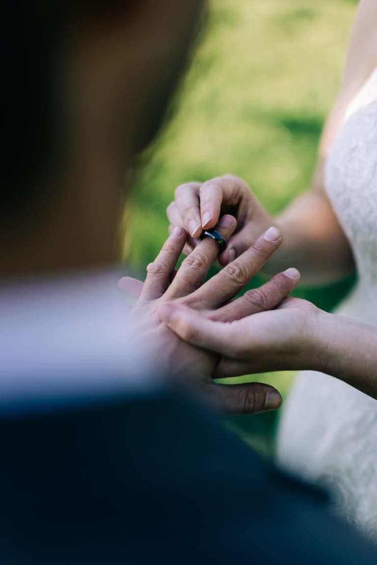 Bride slipping a wedding band onto the groom's finger