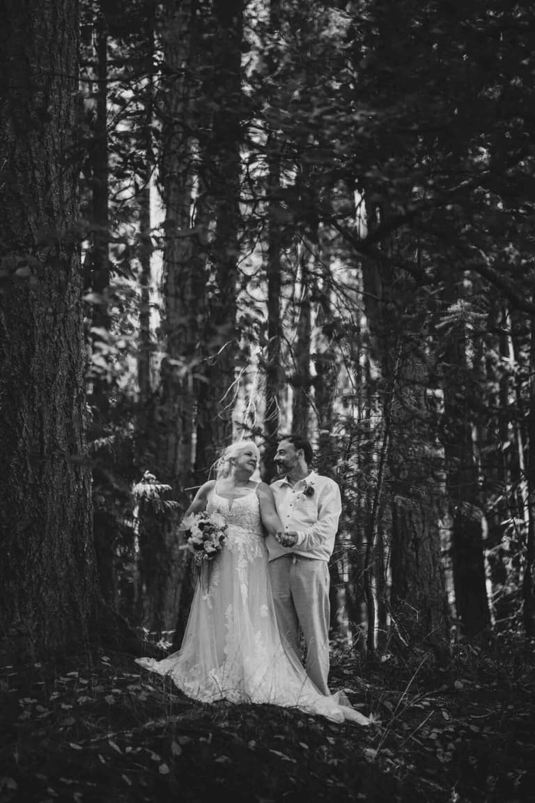 Newlyweds smiling among towering trees in black and white
