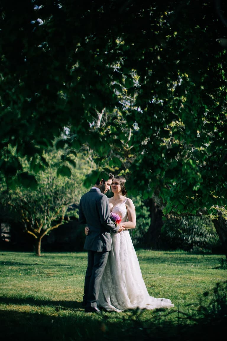 Couple embracing under broad leafy trees on the farm lawn