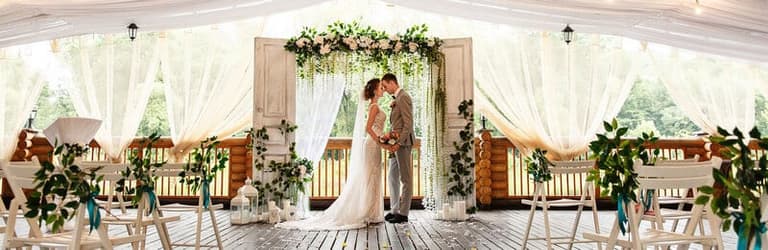 Couple kissing beneath a floral arch inside a draped Special Occasions tent