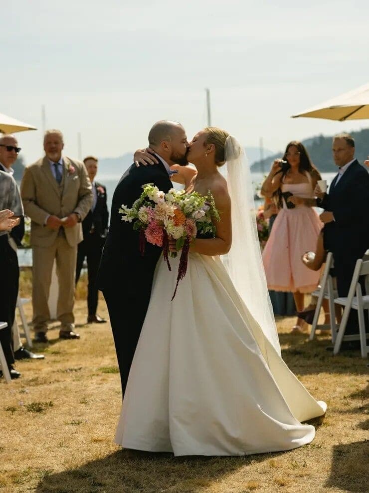 Bride and groom kissing at a waterfront ceremony near moored sailboats