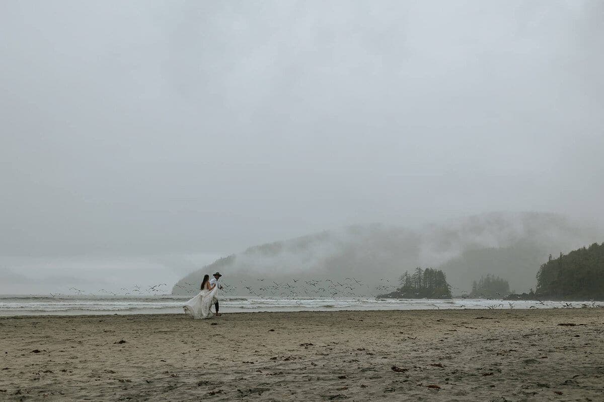 Distant couple crossing a foggy beach as shorebirds take flight