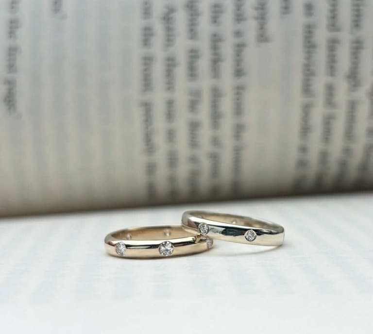 Two diamond-studded gold wedding bands resting against open book pages