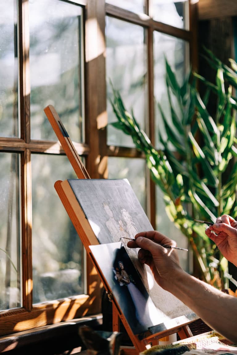 Hand painting a small canvas beside a sunlit studio window