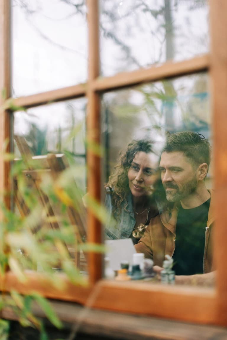 The two artists mixing paints behind a wood-framed studio window