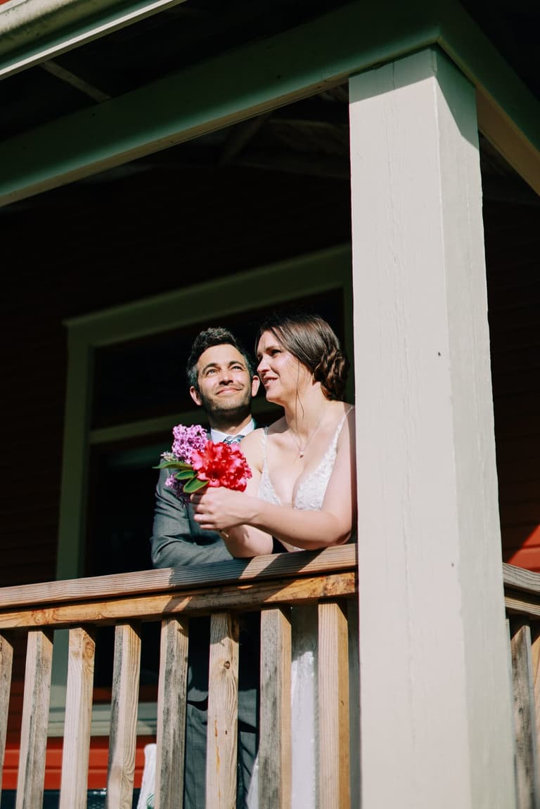 Bride with a pink bouquet leaning on the porch rail