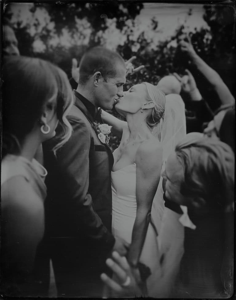 Bride and groom kissing amid a crowd of cheering guests