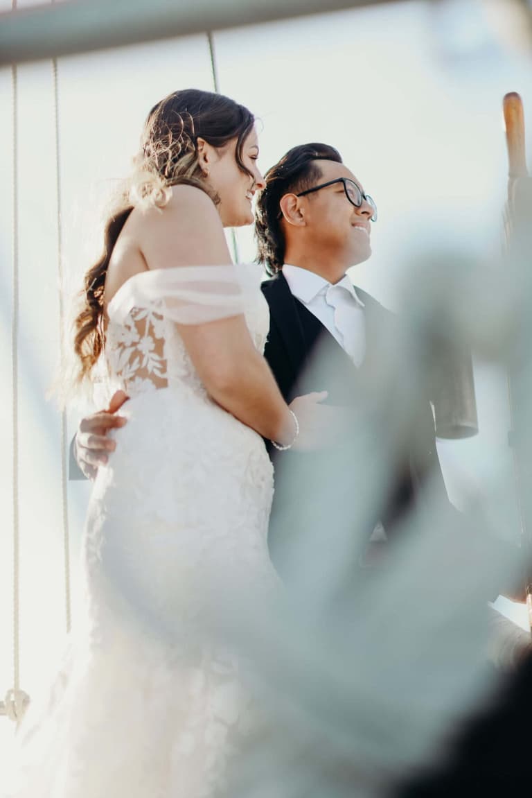 Bride in off-shoulder lace leaning into the seated groom