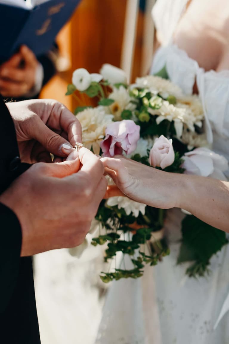 Groom sliding a ring onto the bride's finger over a pastel bouquet