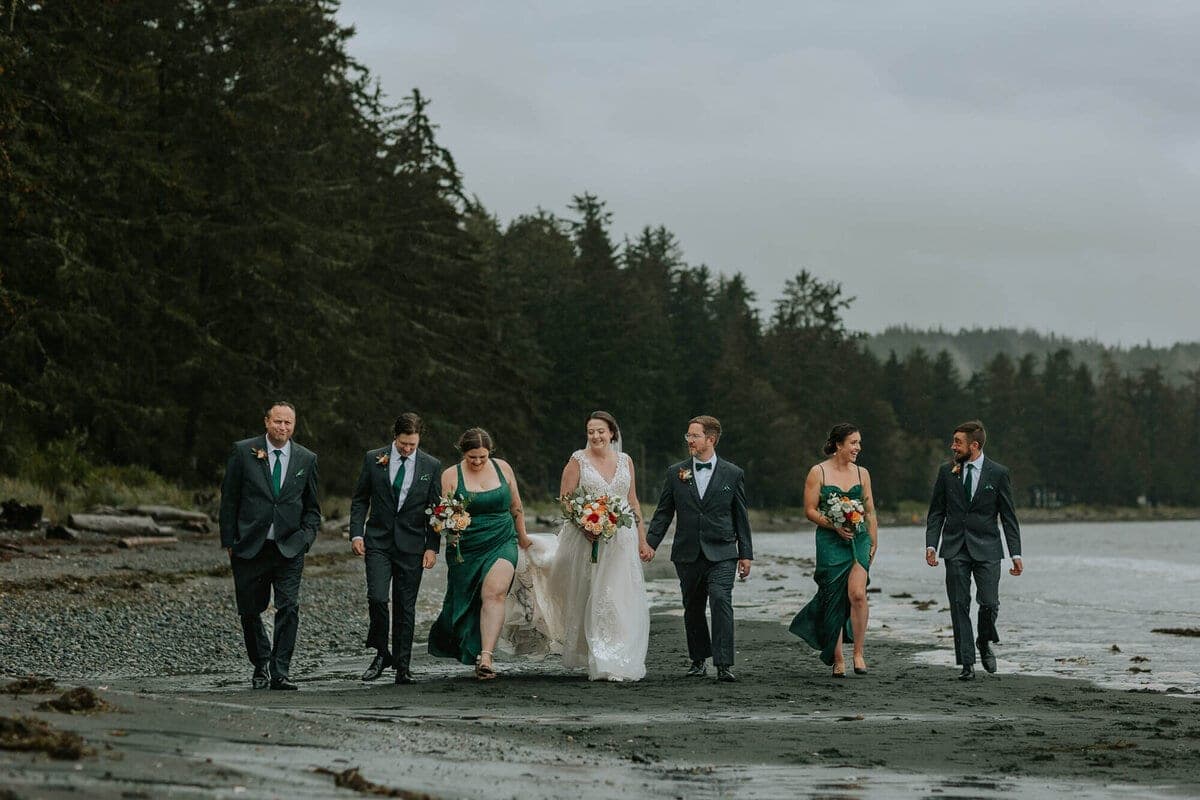 Wedding party in green dresses walking a misty pebble beach