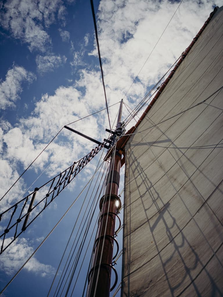 Looking up the varnished mast past ratlines into a cloud-flecked sky