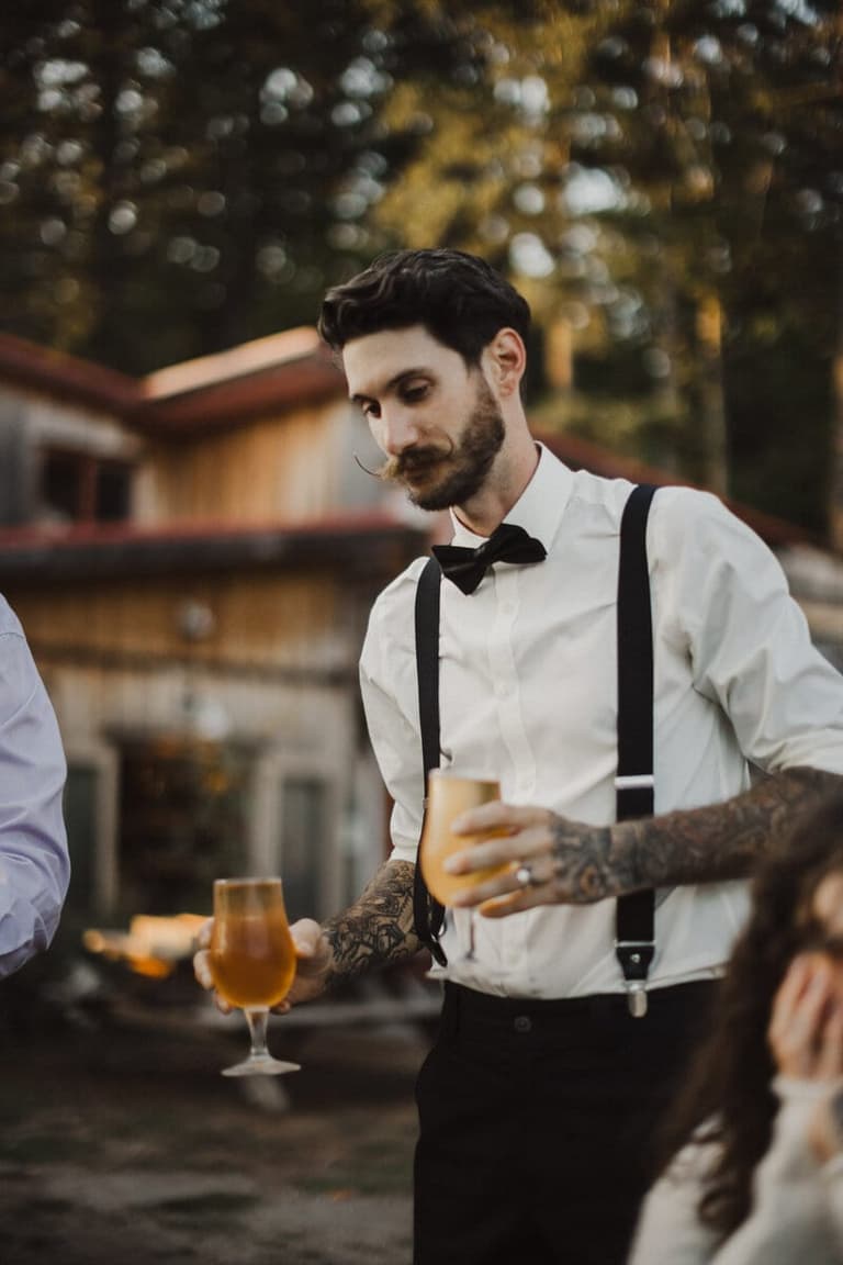 Man in bow tie and suspenders carrying two glasses of cider
