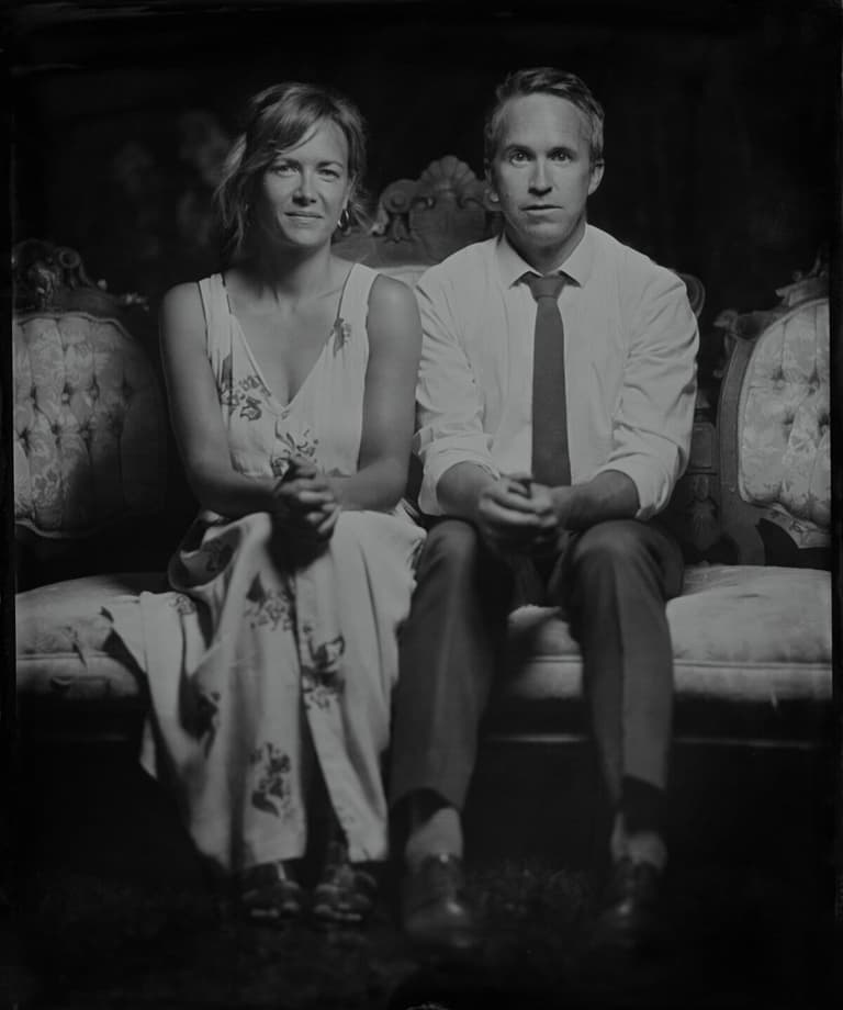 Couple in summer attire seated on a Victorian sofa, tintype