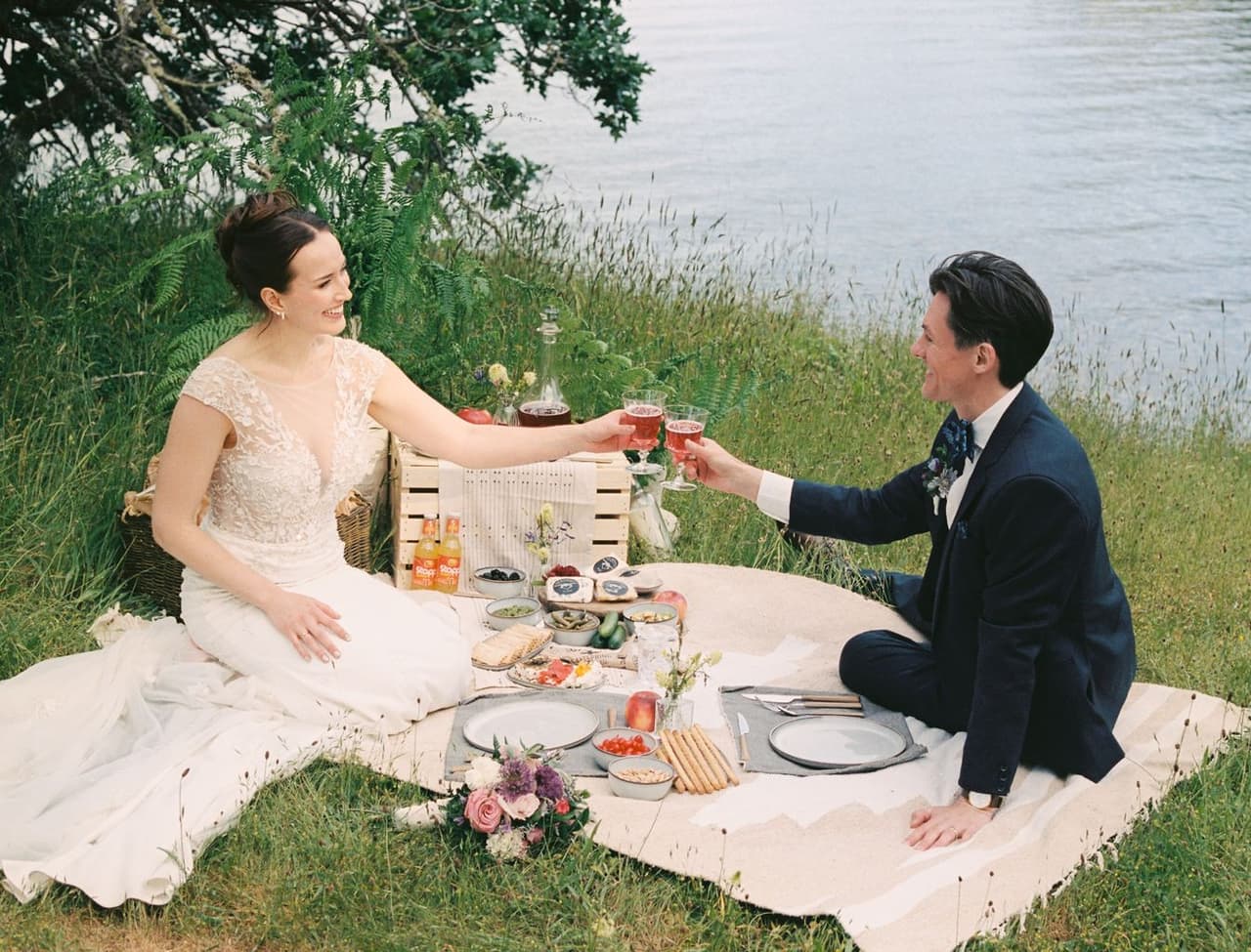 Two people toast with rosé over a picnic spread at the water's edge on Salt Spring Island