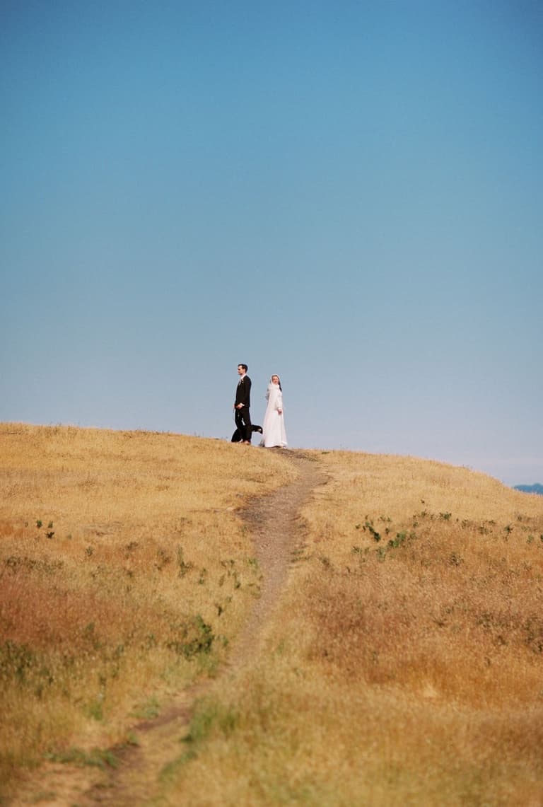 Newlyweds trailing hands along leafy vineyard rows