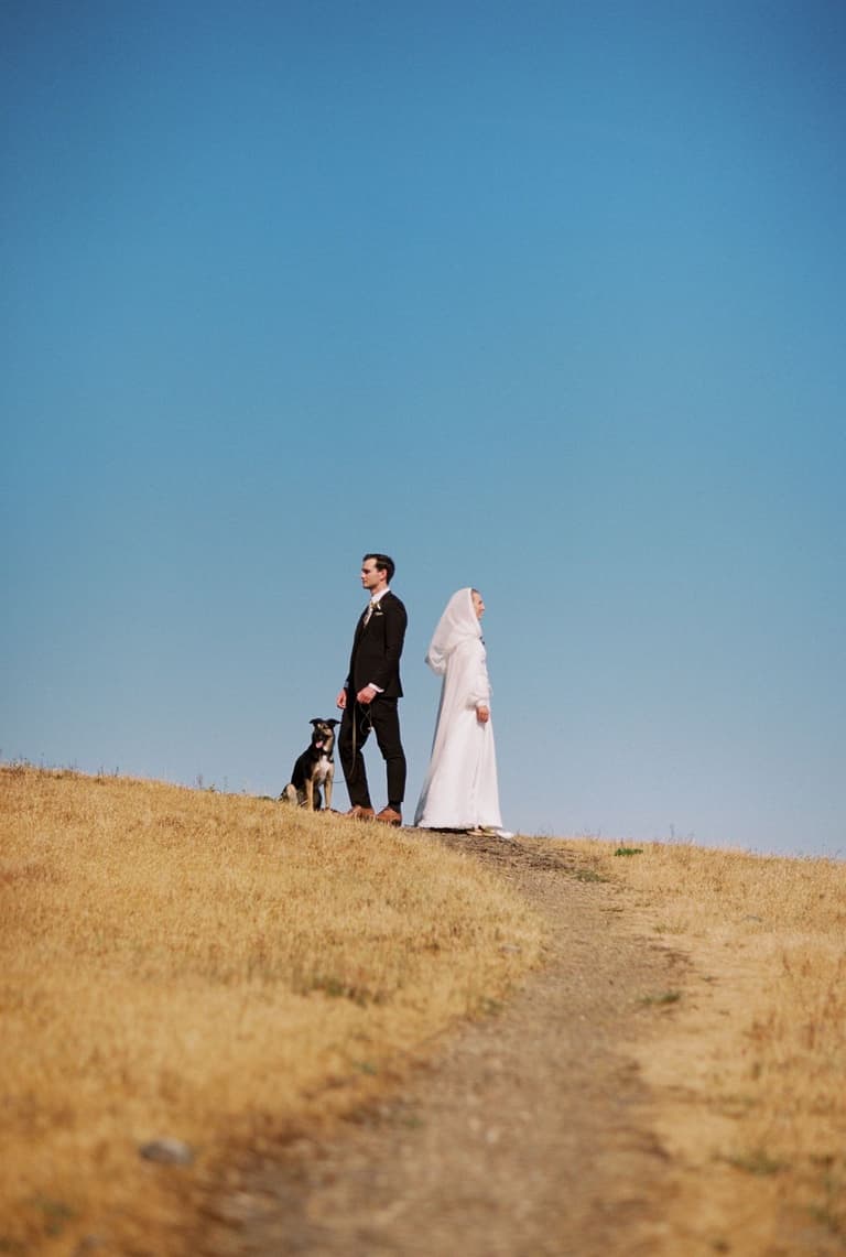 newlyweds pausing on a narrow path through sunlit birch forest