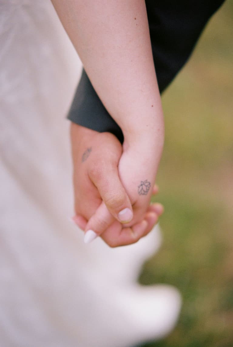 Two people holding hands, one wearing a dark sleeve with a small leaf tattoo visible on their wrist
